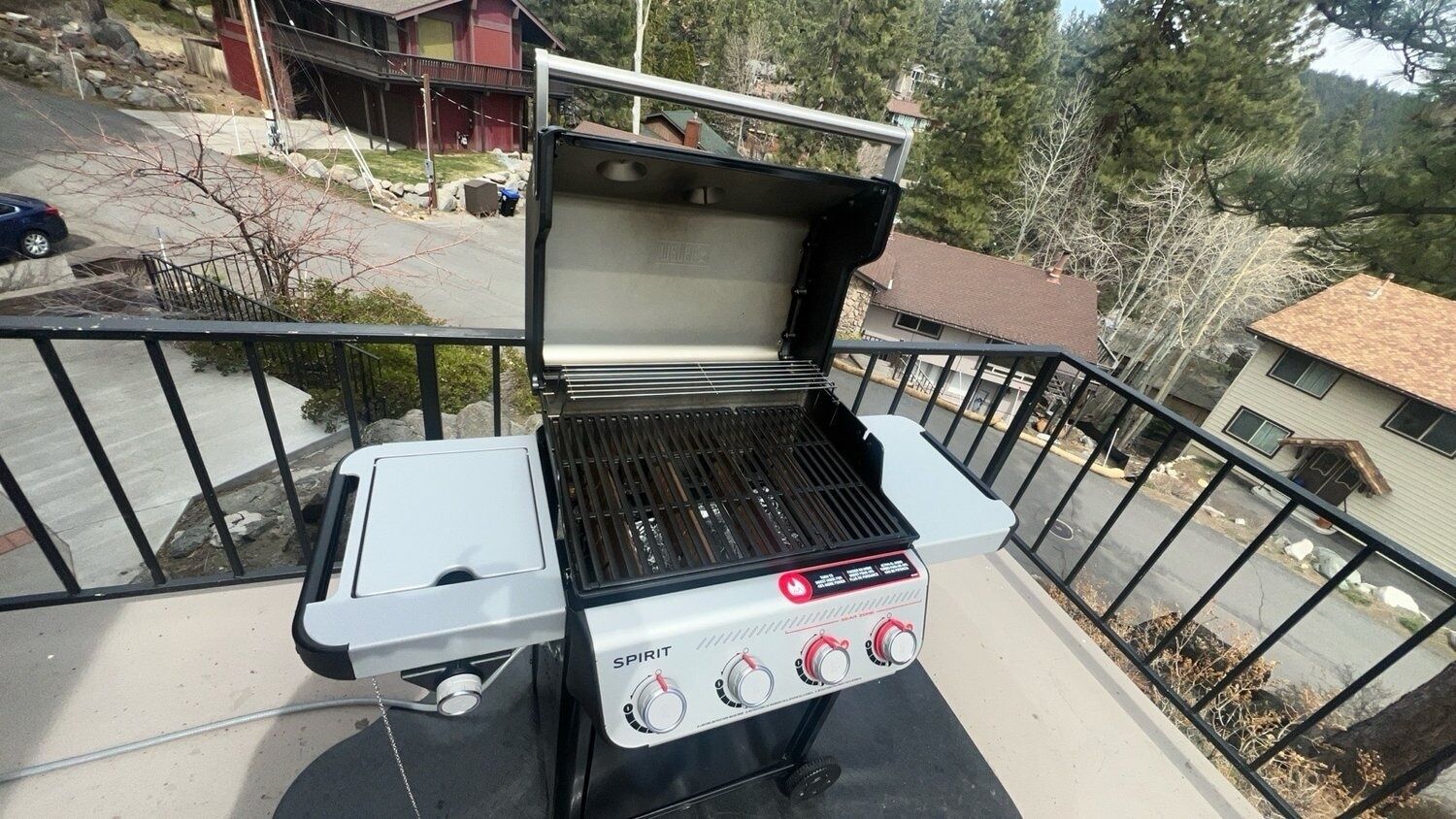 Ein Spirit tragbarer Grill auf einem Balkon mit Metallgeländer, Blick auf eine Wohngegend und ein Haus im Hintergrund.