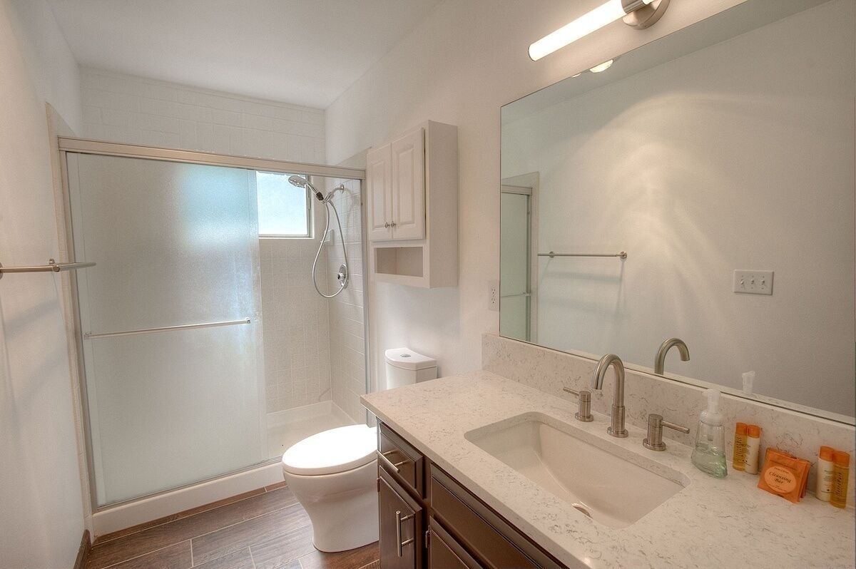 A modern bathroom with a glass-enclosed shower, a white toilet, a sink with a mirror, and a countertop with toiletries.