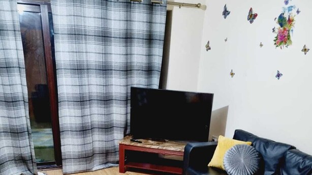 Ett vardagsrum med en svart soffa, ett soffbord i trä, en rutig gardin och en mönstrad matta.
