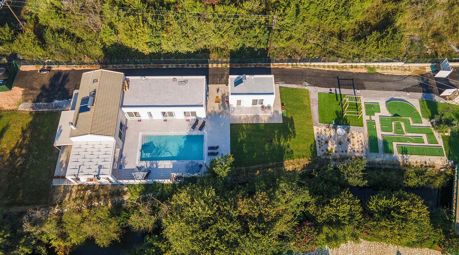 An aerial view of a property with a swimming pool, a large building with a sloped roof, and a well-maintained lawn with a maze garden.