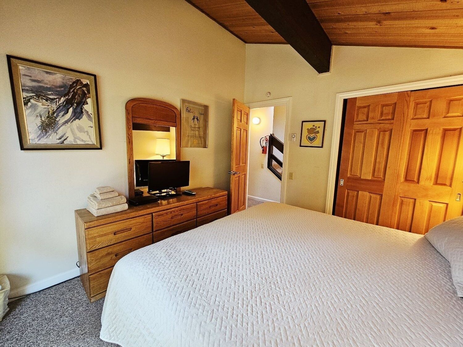 Habitación de hotel con una cama grande, cómoda de madera, televisor y un cuadro enmarcado en la pared.