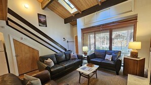 A spacious living room with two leather sofas, a coffee table, and a wooden cabinet. There is a staircase with black railings and a skylight above. - Cartwright Corner Condo 4 Bedroom Townhouse by RedAwning (Incline Village)