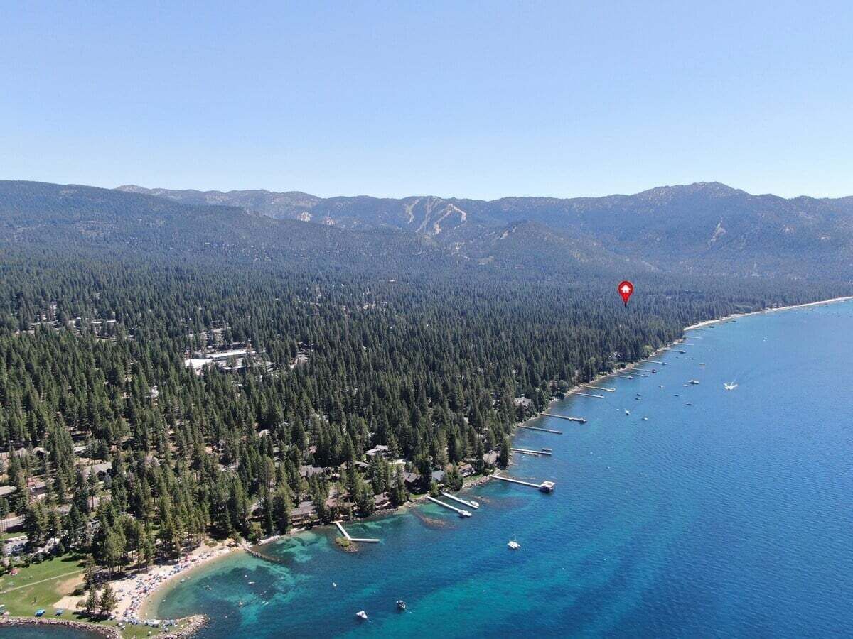 An aerial view of a coastal area with dense forest, clear blue waters, and a red location marker.