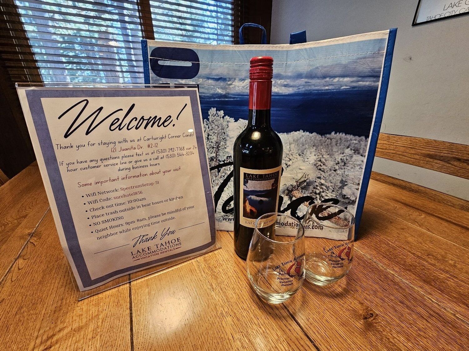 A welcome sign with a bottle of wine and two glasses on a wooden table.