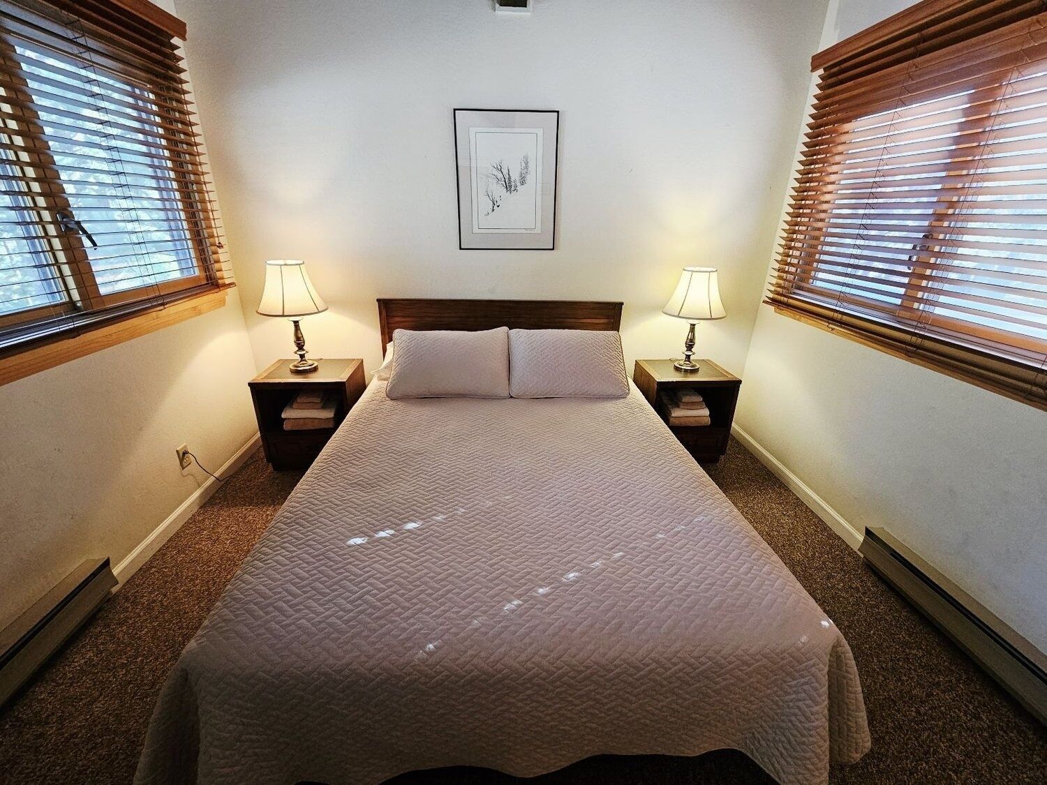 Une chambre à coucher bien aménagée, avec un grand lit, deux tables de chevet avec des lampes et des stores en bois aux fenêtres.