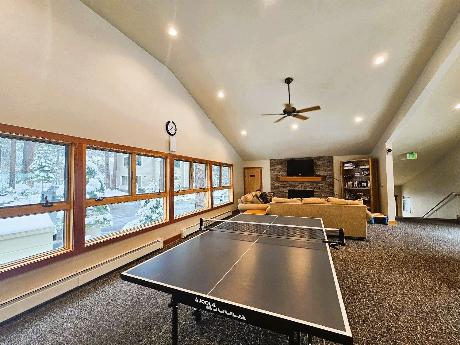 Une table de ping-pong dans une pièce dotée de grandes fenêtres, d’un ventilateur de plafond et d’une cheminée.