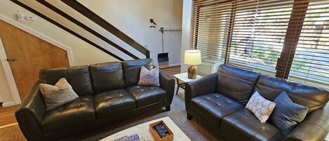 A living room with two black leather sofas, a coffee table with magazines, and a lamp.