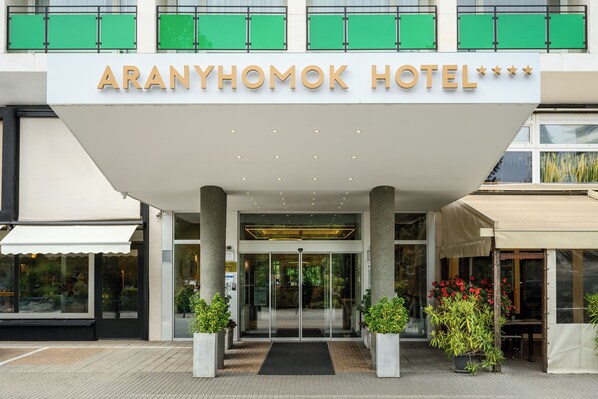 The Aranyhomok Hotel entrance with a modern design, featuring a large overhang, glass doors, and potted plants. - Aranyhomok Hotel Business & Relax (Kecskemet)