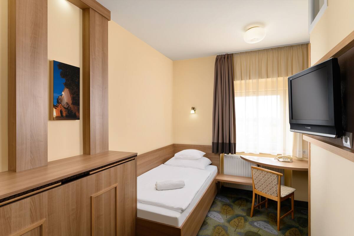 Habitación de hotel con cama, escritorio con silla, televisor y un cuadro en la pared.
