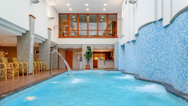 Una piscina con una fuente de agua, sillas amarillas y una zona de recepción con un cartel.