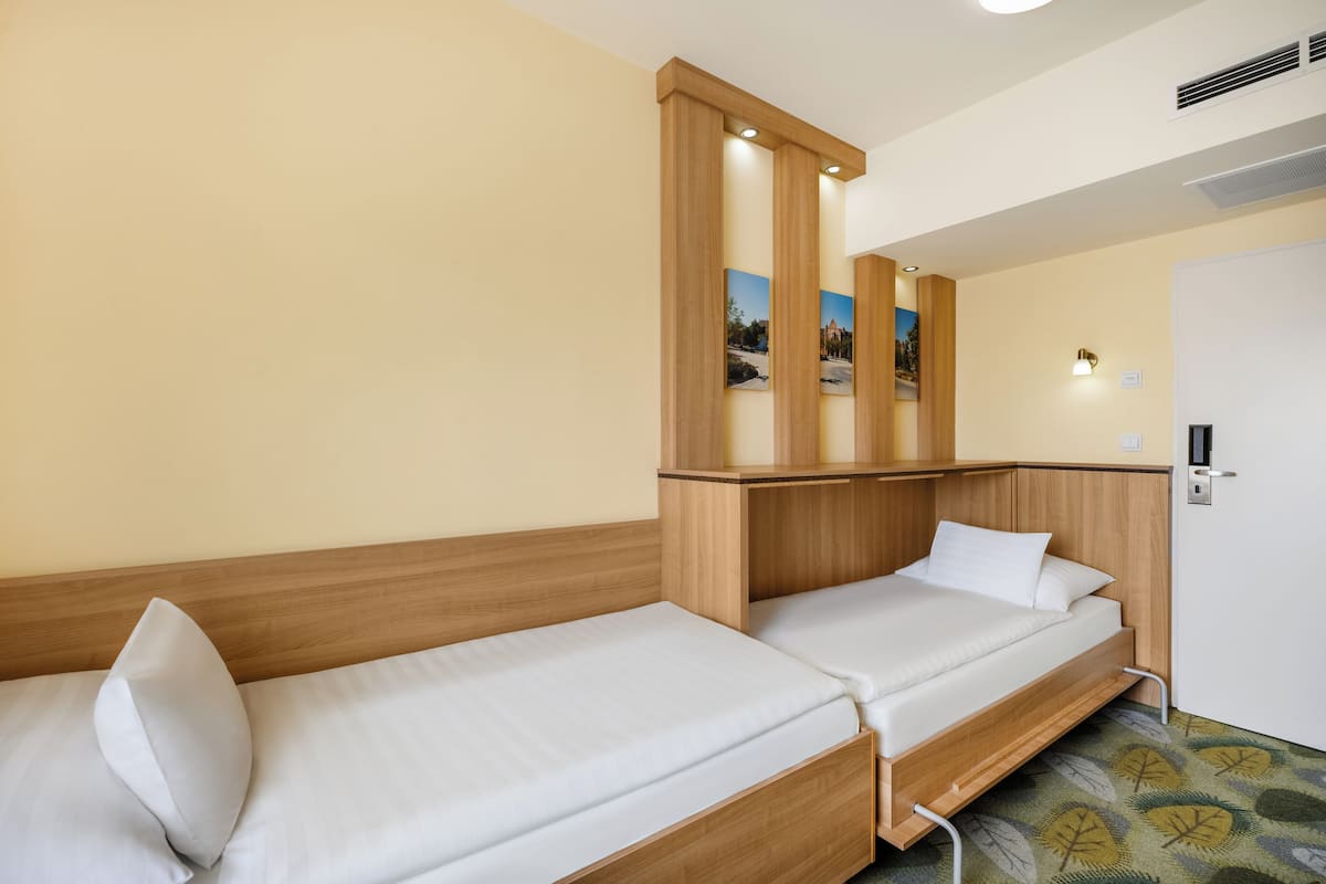 Habitación de hotel con dos camas individuales, cabeceros de madera, un televisor pequeño de pared y una puerta con pomo.