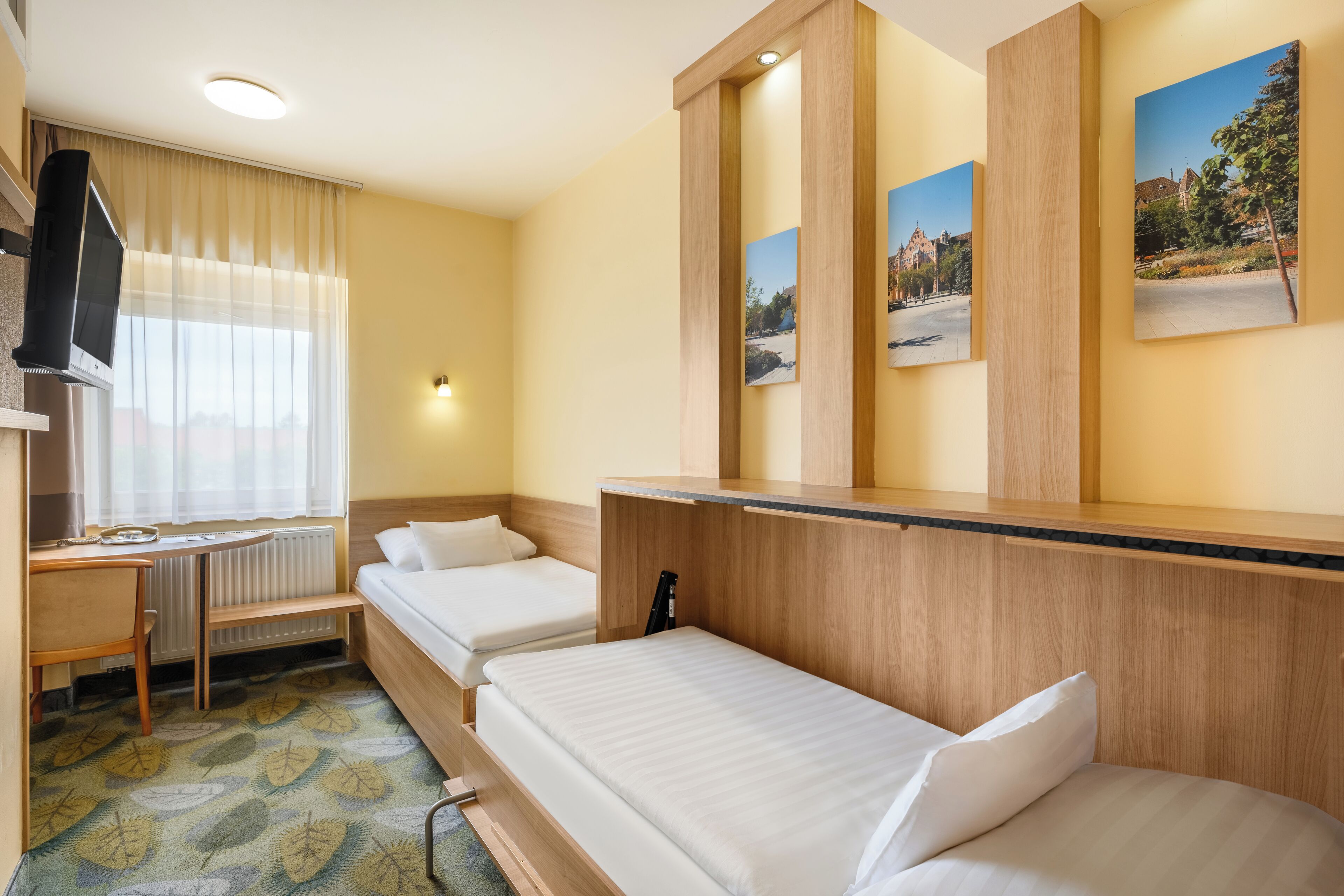 A hotel room with two single beds, a desk with a chair, a flat-screen TV, and a radiator.
