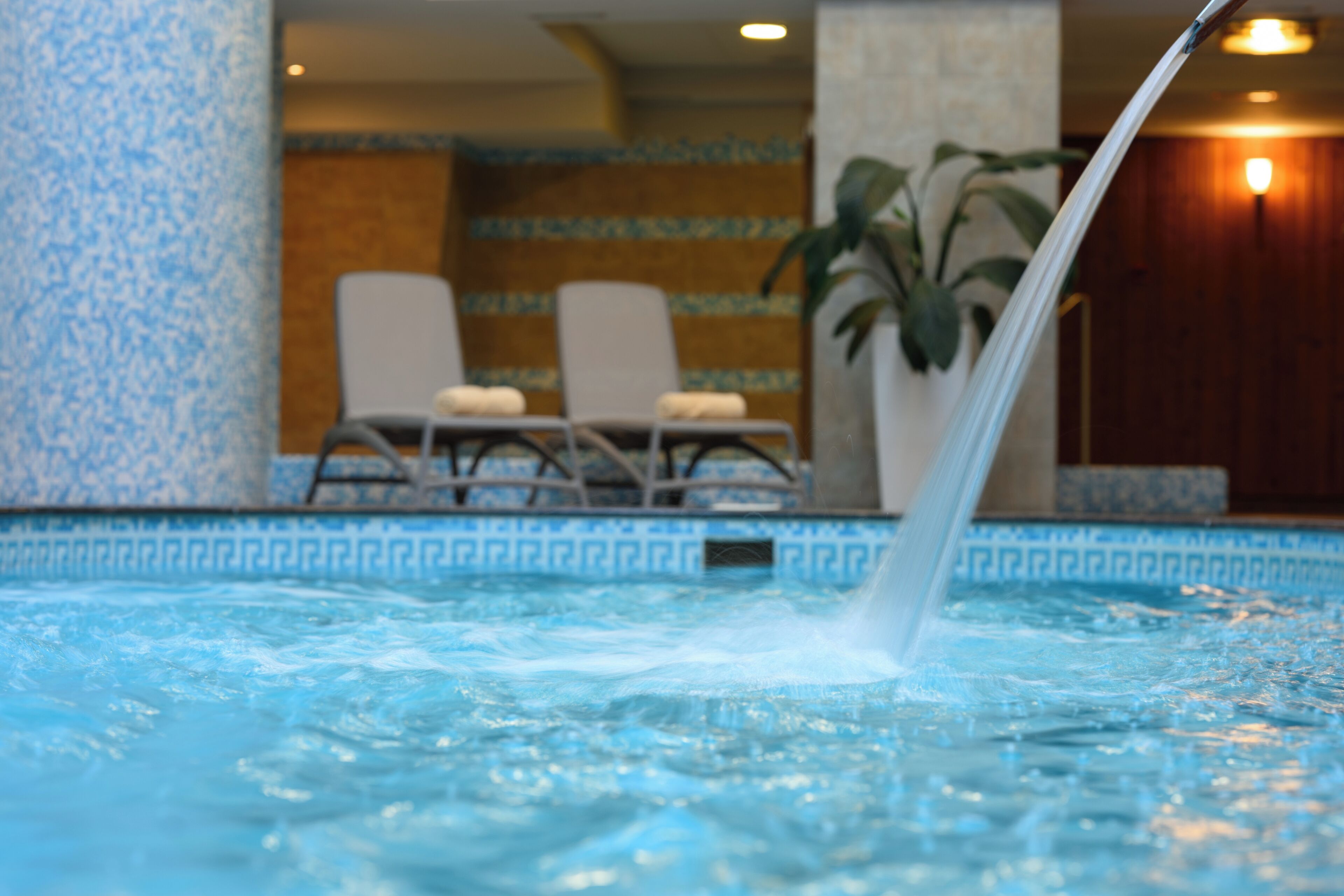 Une piscine dotée de jets d’eau, de chaises longues et d’un mur décoré d’un motif particulier en arrière-plan.
