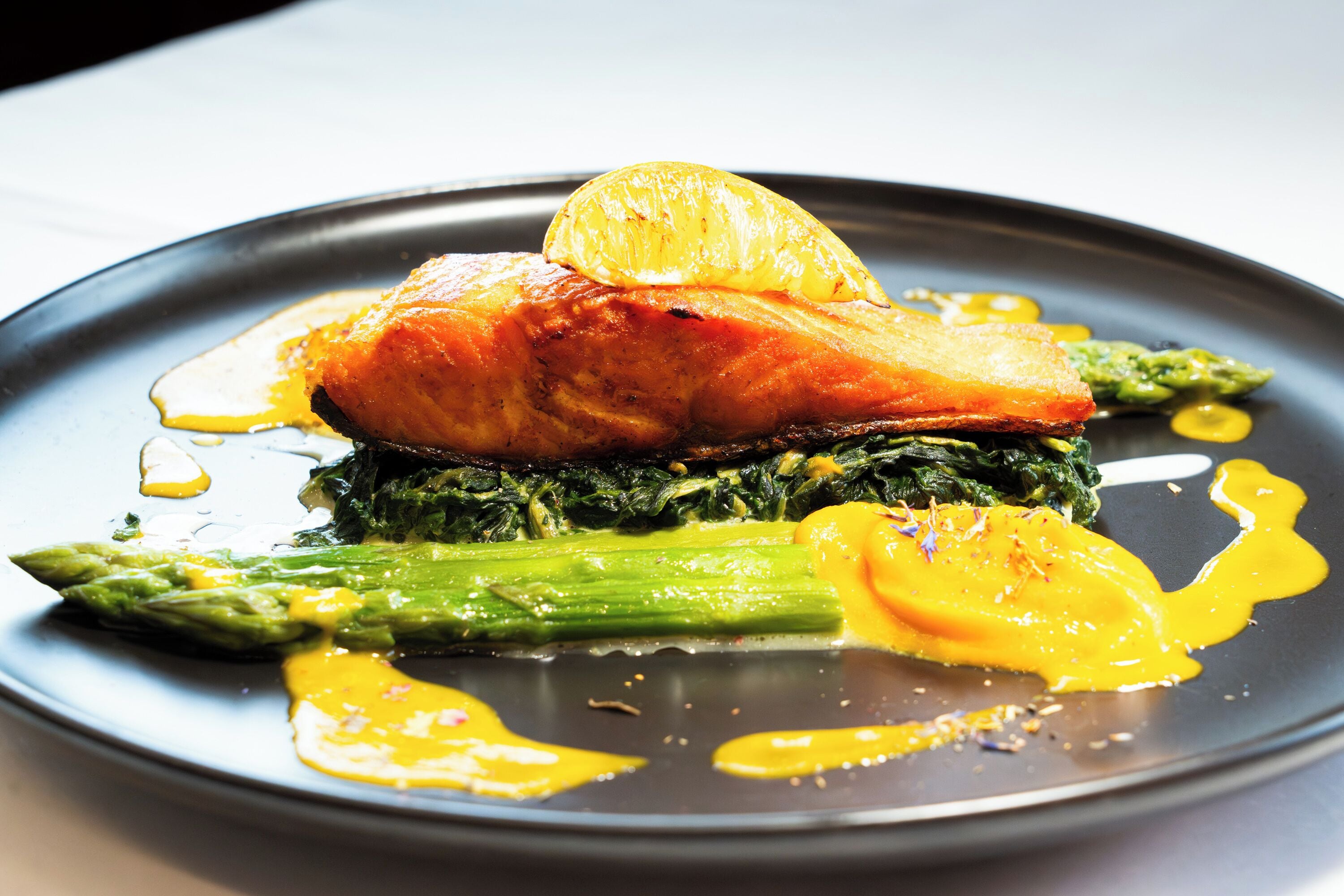 A plate of food with salmon, asparagus, and a lemon slice.