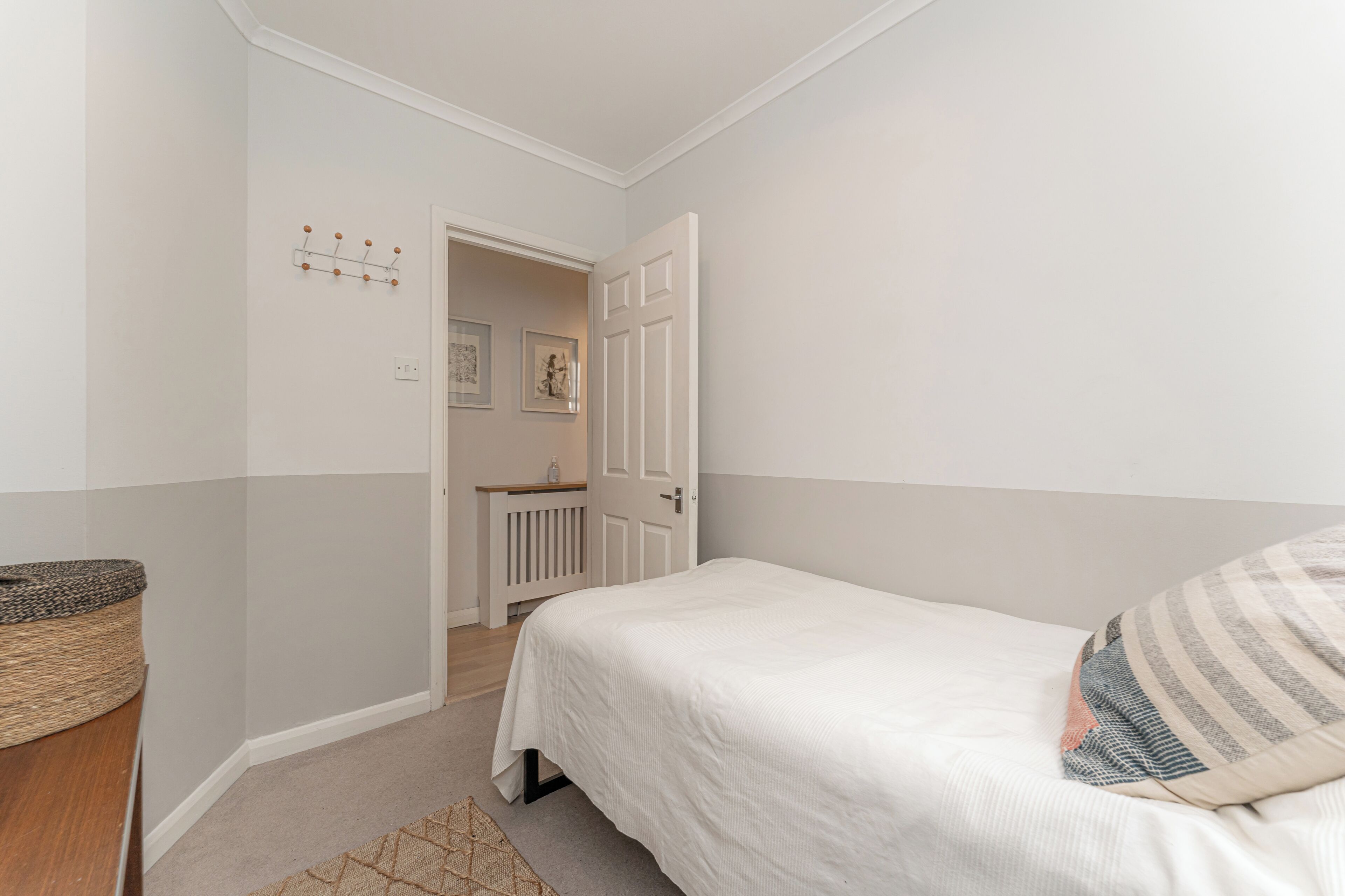 A bedroom with a bed, a door, a small table, and a wall-mounted coat rack.