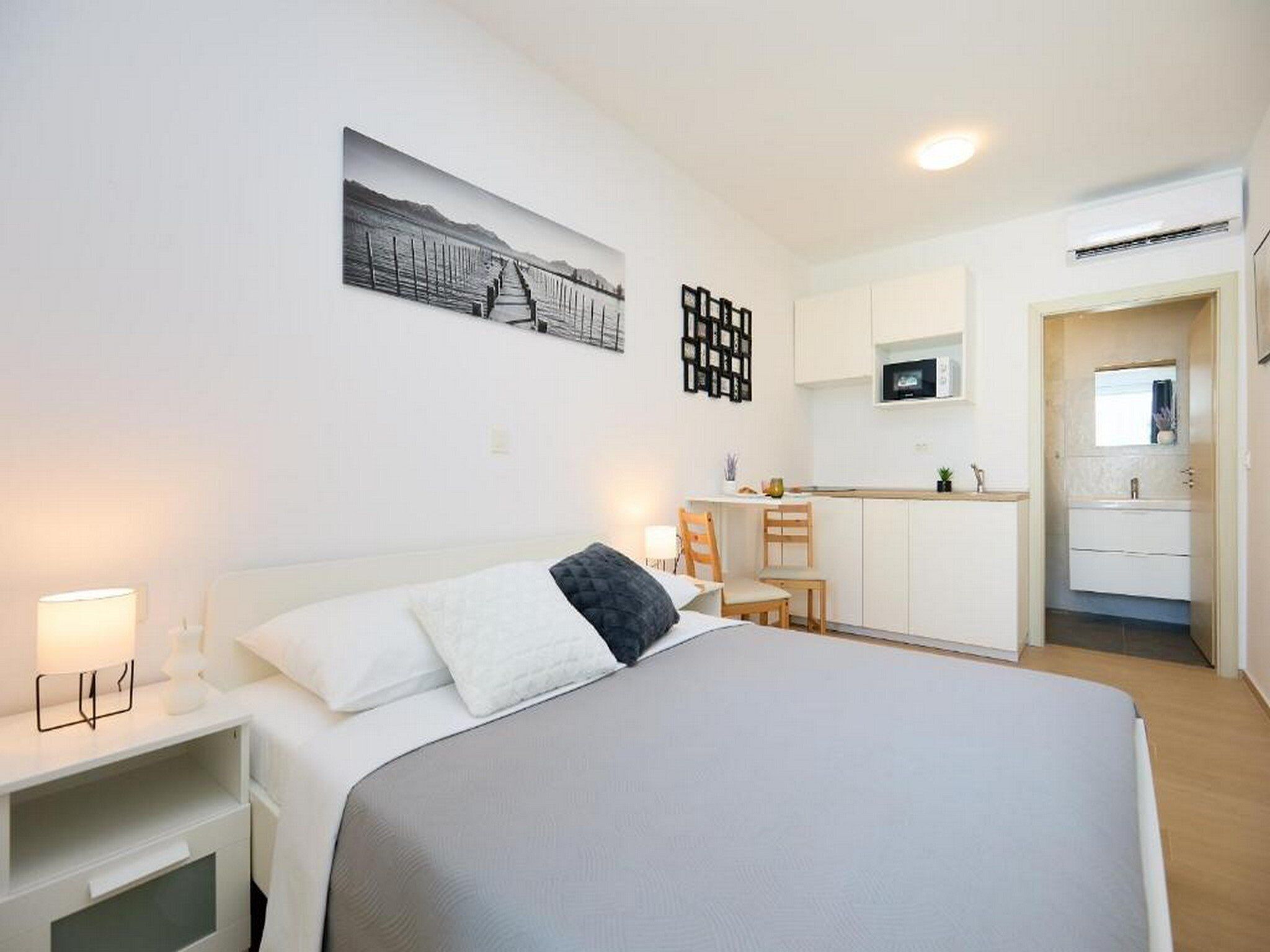 A modern hotel room with a bed, bedside tables, a desk, and a kitchenette.