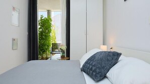 A bedroom with a bed, a nightstand, a window with curtains, a potted plant, and a view of the outside. - Palm Tree Apartments (Dubrovnik)