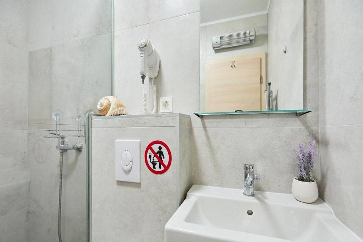 A bathroom with a shower, a sink, a hairdryer, and a no-entry sign.