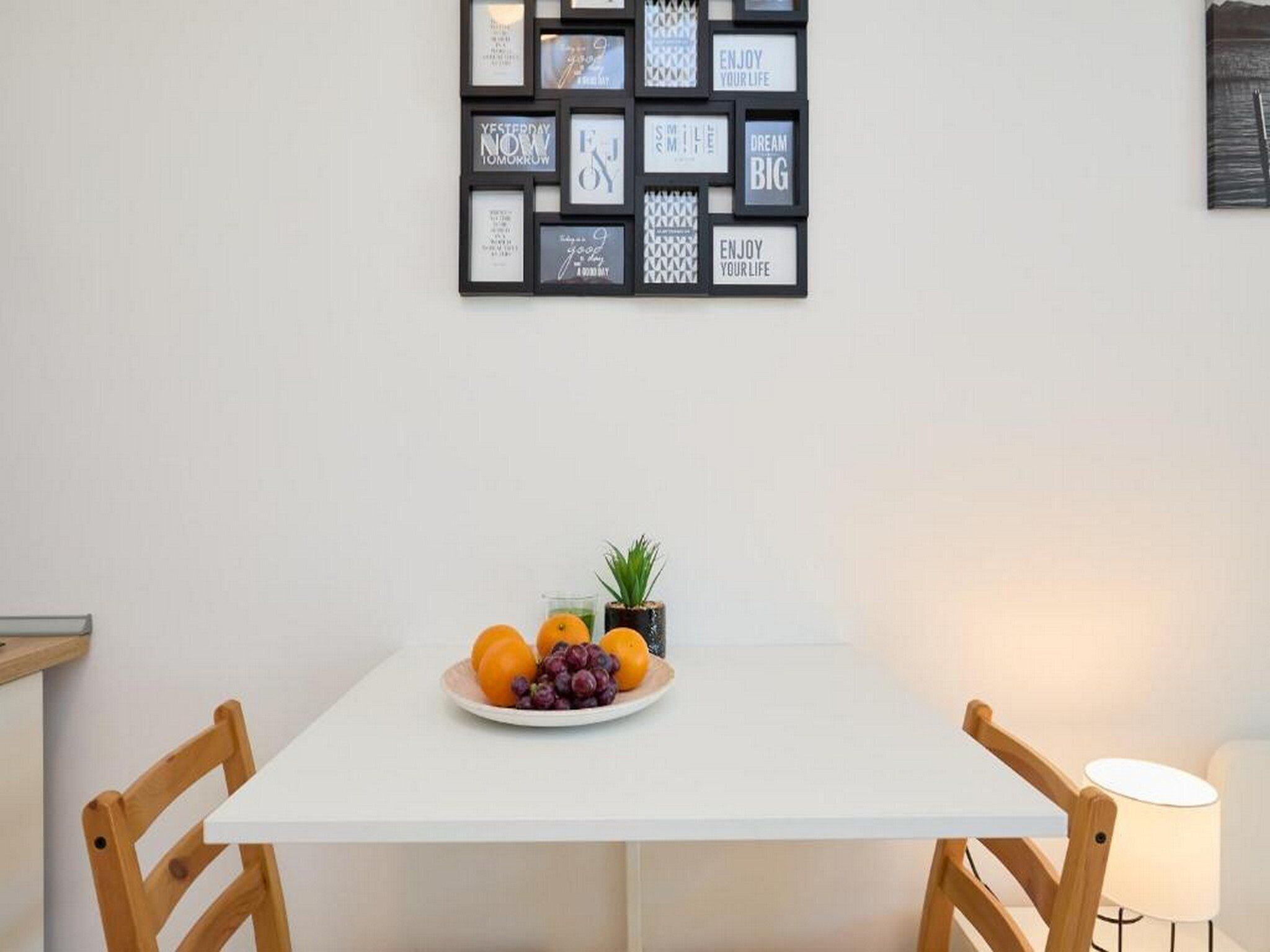 A dining area with a white table, two wooden chairs, a plate of fruit, and a small potted plant.
