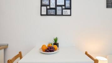 A dining area with a white table, two wooden chairs, a plate of fruit, and a small potted plant.