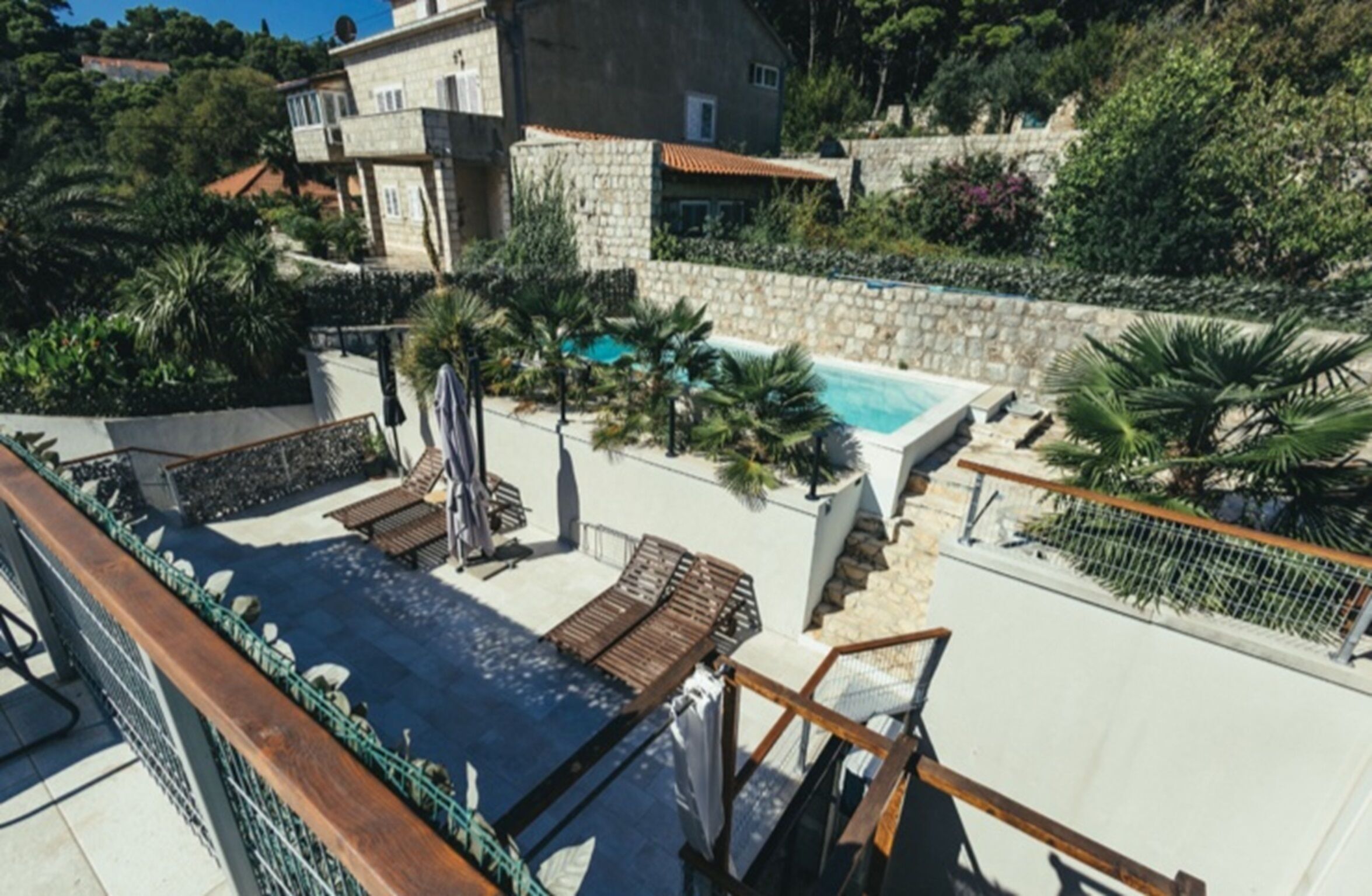 Un área de piscina en la azotea con sillones de descanso y un muro de piedra.