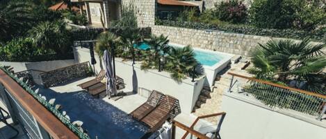 Un área de piscina en la azotea con sillones de descanso y un muro de piedra.