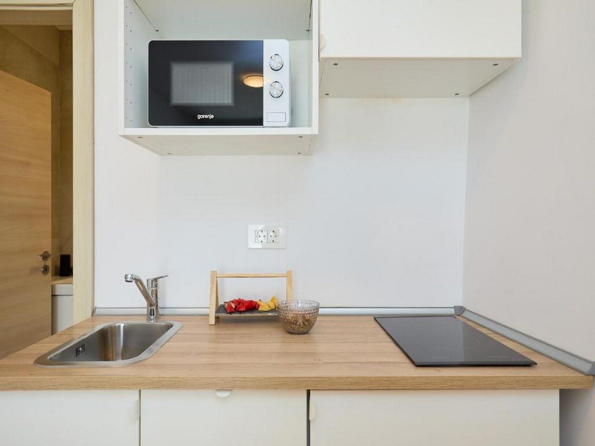 A compact kitchen with a built-in microwave, a stainless steel sink, and a wooden countertop.