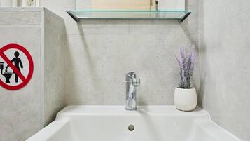 A bathroom with a white sink, a glass shelf above it, and a no-smoking sign.