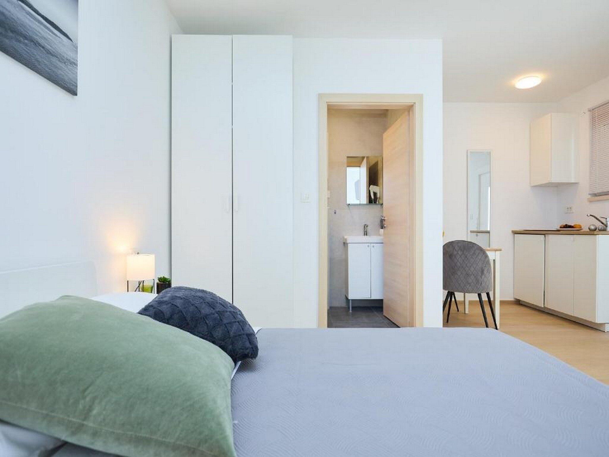 A hotel room with a bed, a chair, a desk, and a kitchenette.