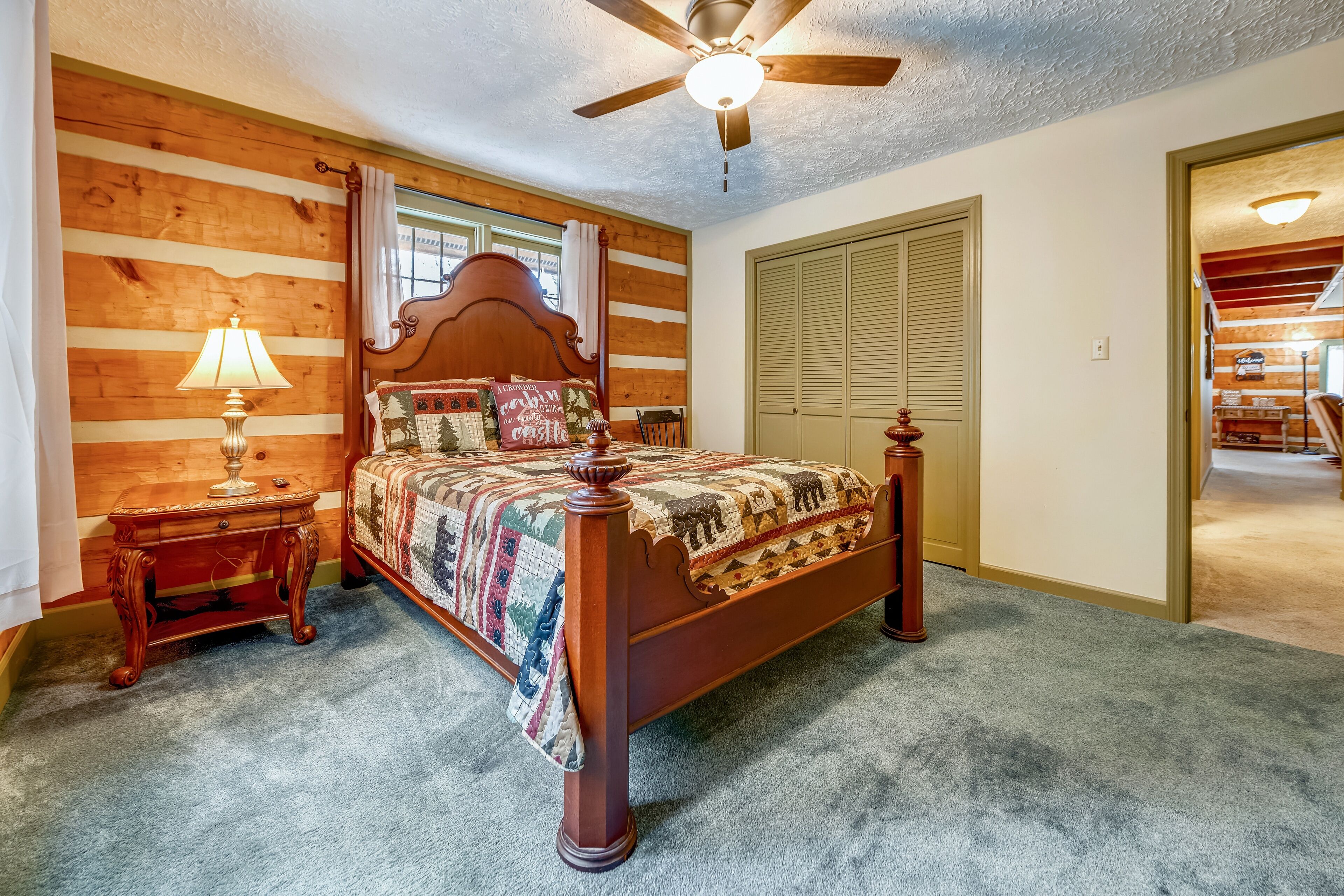 A bedroom with a wooden bed, a nightstand with a lamp, a ceiling fan, and a closet.