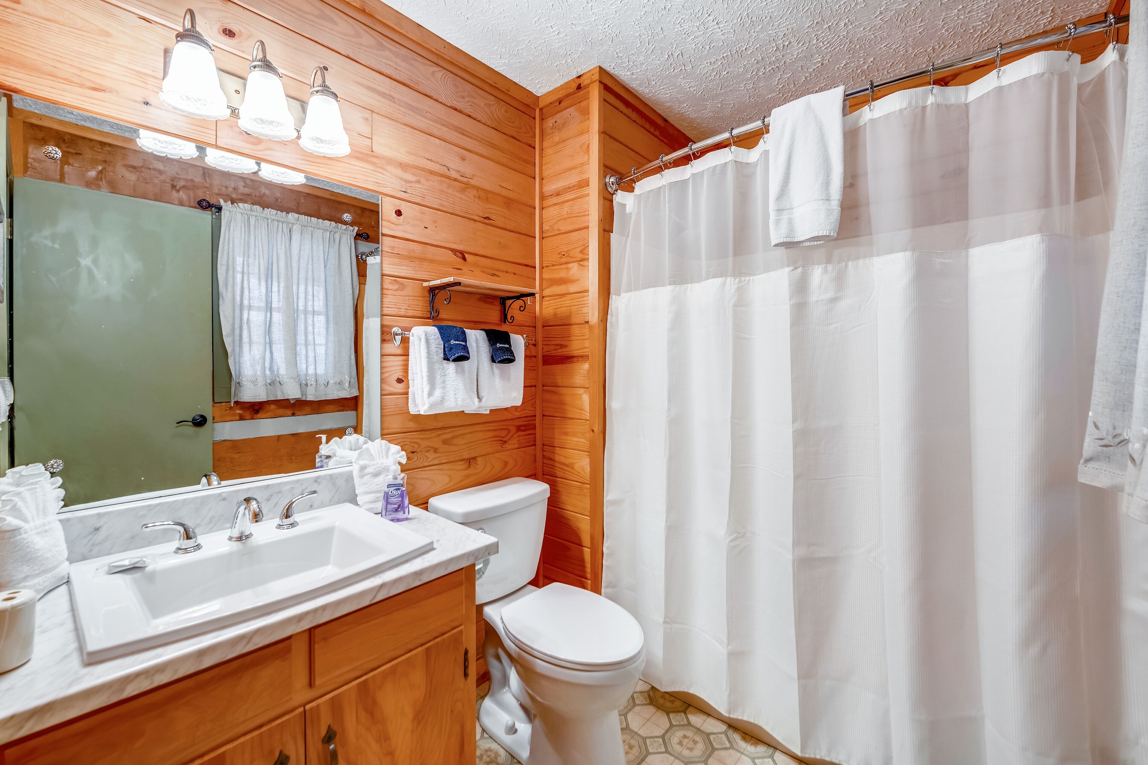 A bathroom with wooden walls, a white sink, a toilet, and a shower curtain.