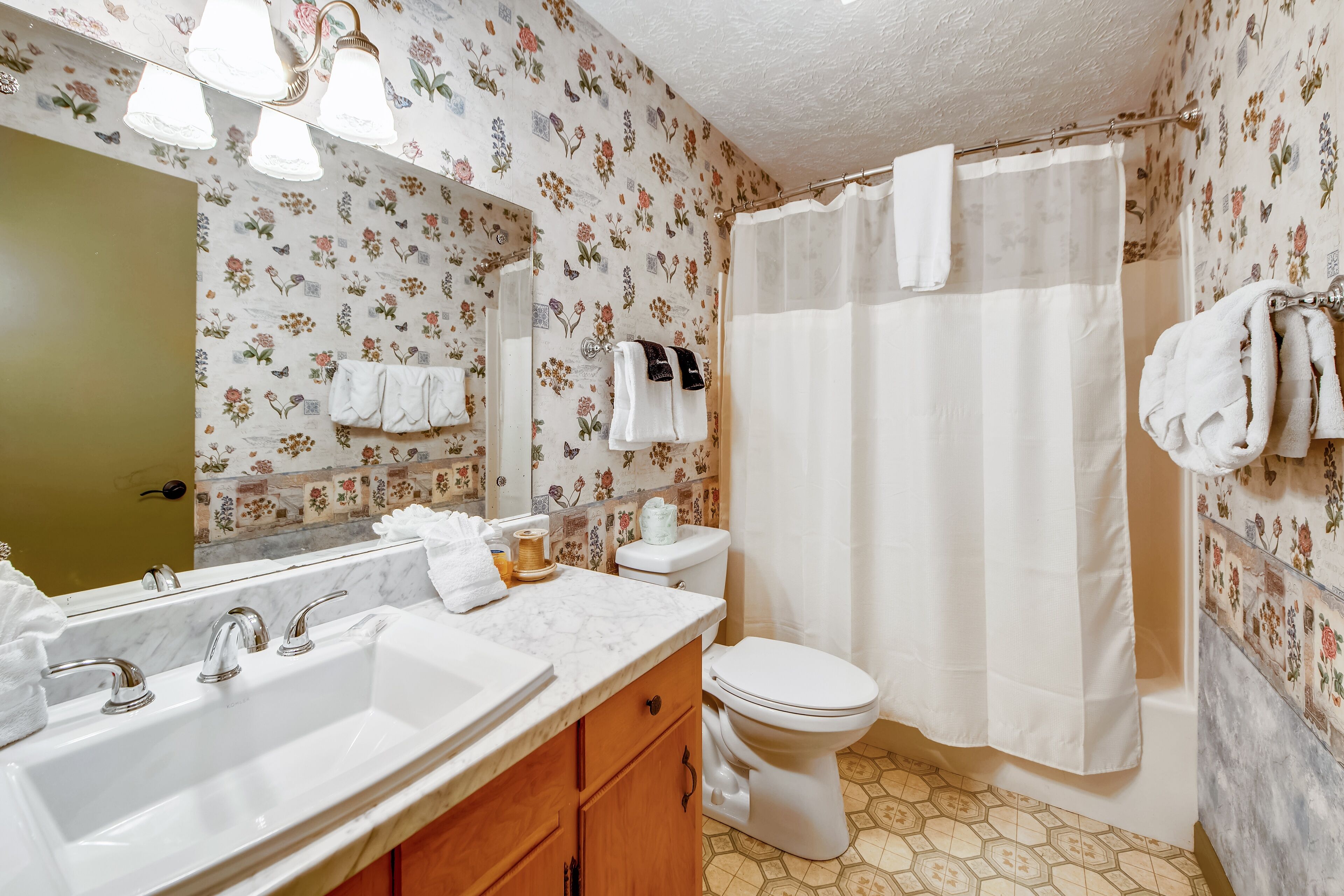 A bathroom with a sink, mirror, toilet, and shower curtain.