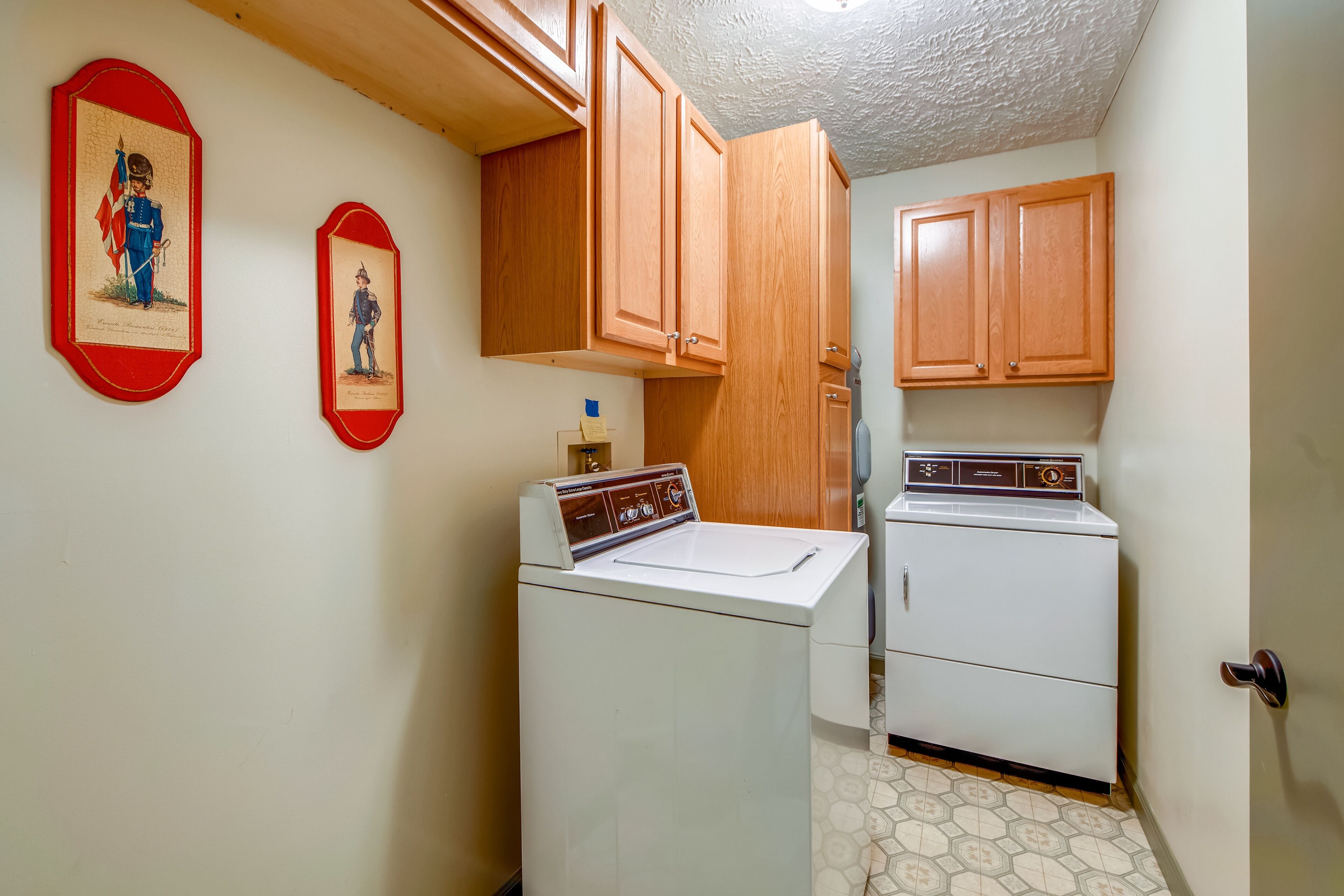 A laundry room with wooden cabinets, a washing machine, and two framed pictures on the wall.