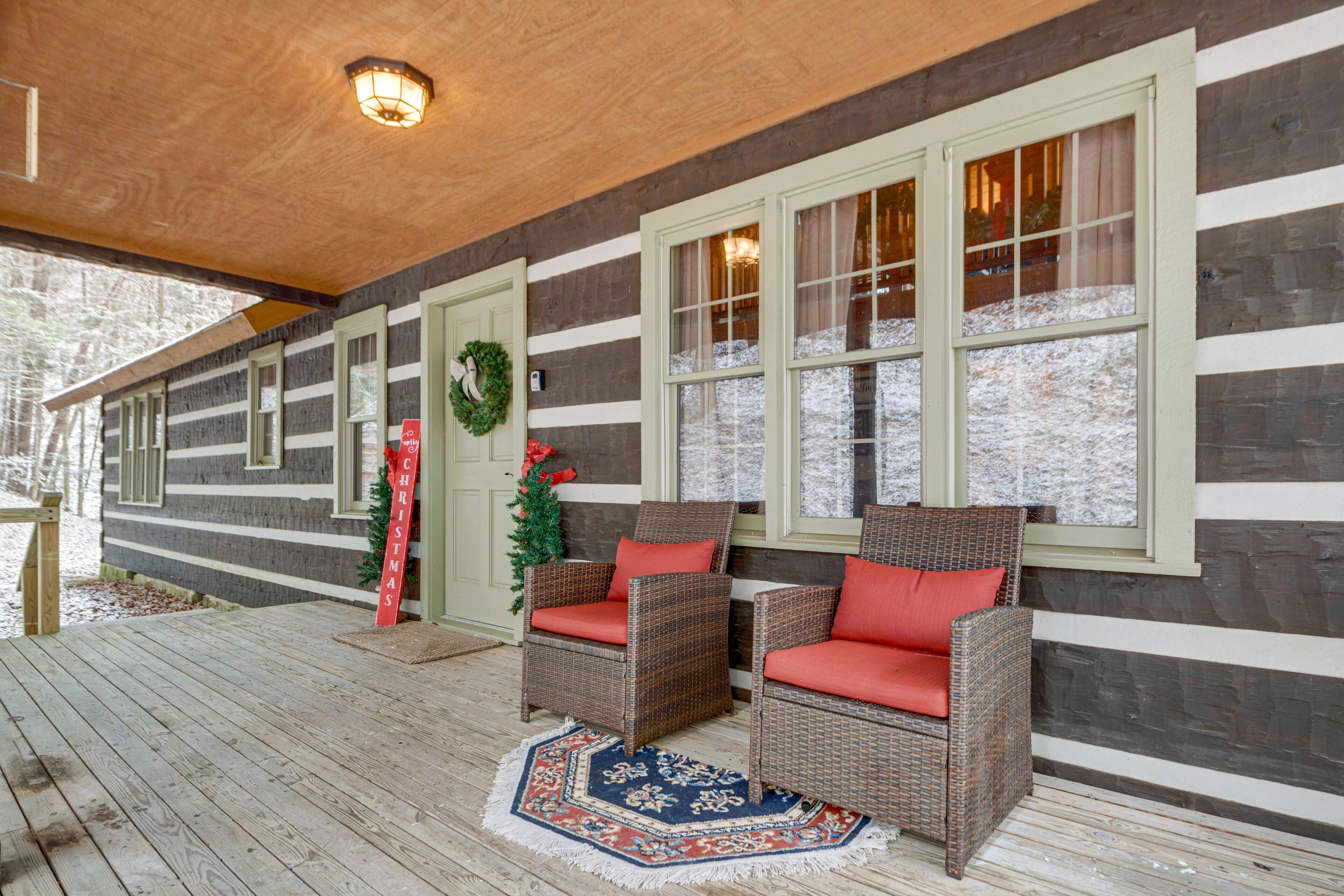Une cabane en rondins avec deux fauteuils en osier dotés de coussins rouges, une couronne de Noël et une terrasse en bois.