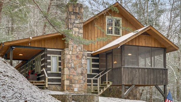 Een chalet met een stenen schoorsteen, houten gevel en een balkon met uitzicht op het omliggende bos.