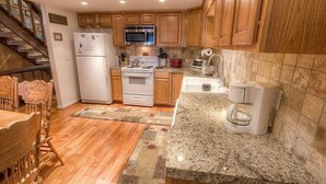 A kitchen with wooden cabinets, a stainless steel microwave, a white refrigerator, a stove, and a coffee maker.