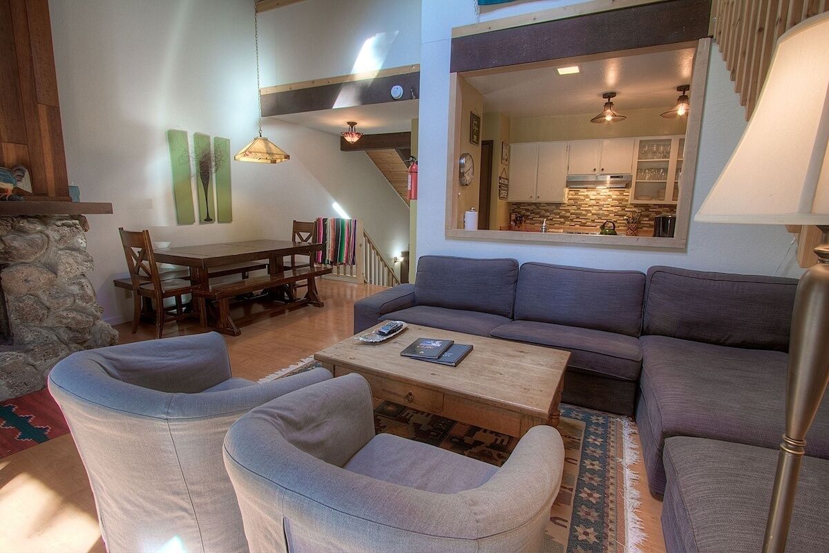 A modern living room with a gray sofa, two armchairs, a wooden coffee table, and a dining area with a wooden table and chairs.