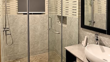 A modern bathroom with a glass-enclosed shower, a large mirror, and a marble-tiled floor.