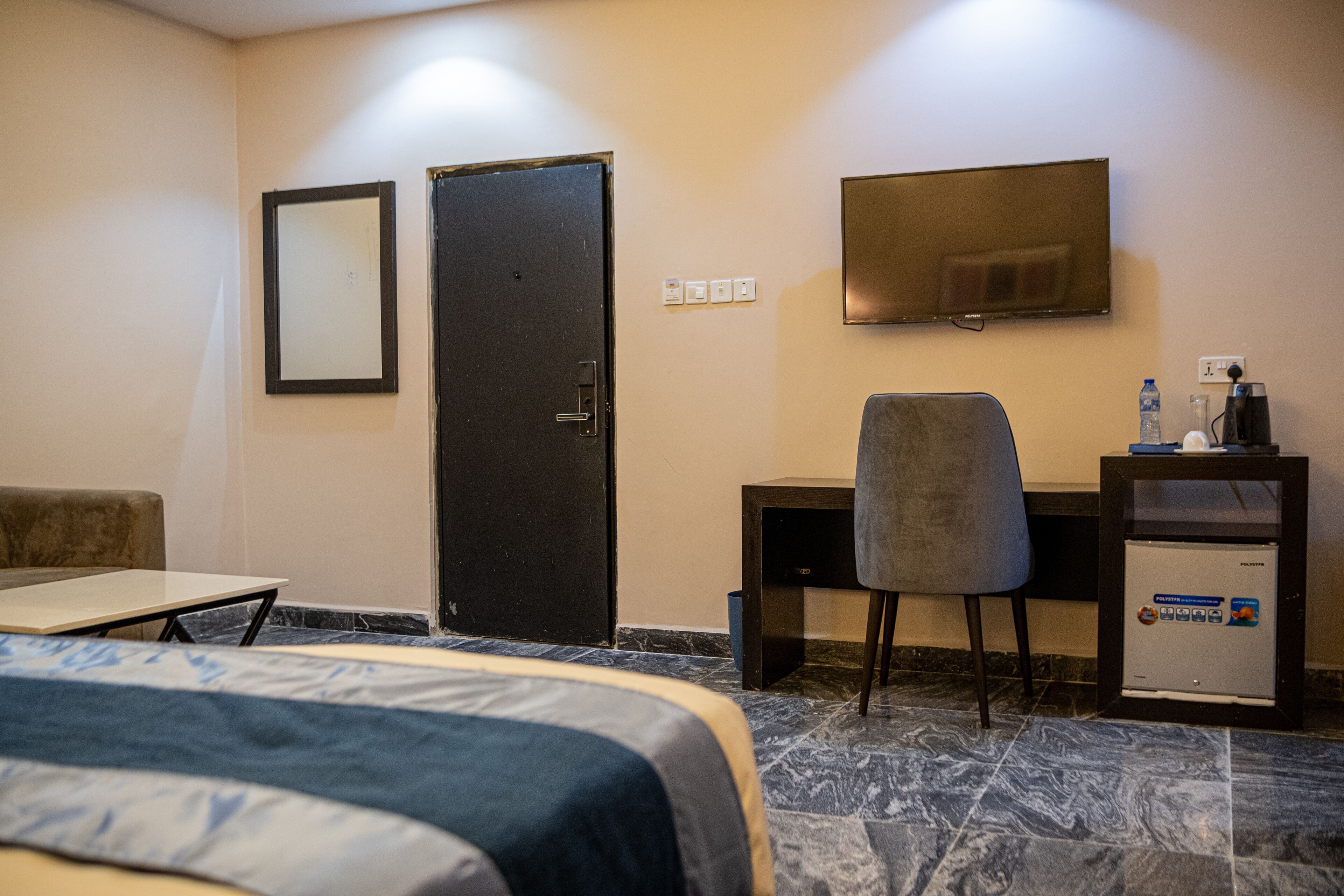 A hotel room with a bed, a desk, a chair, a television, and a minibar.