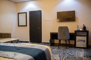 Habitación de hotel con cama, escritorio, silla, televisor y minibar.
