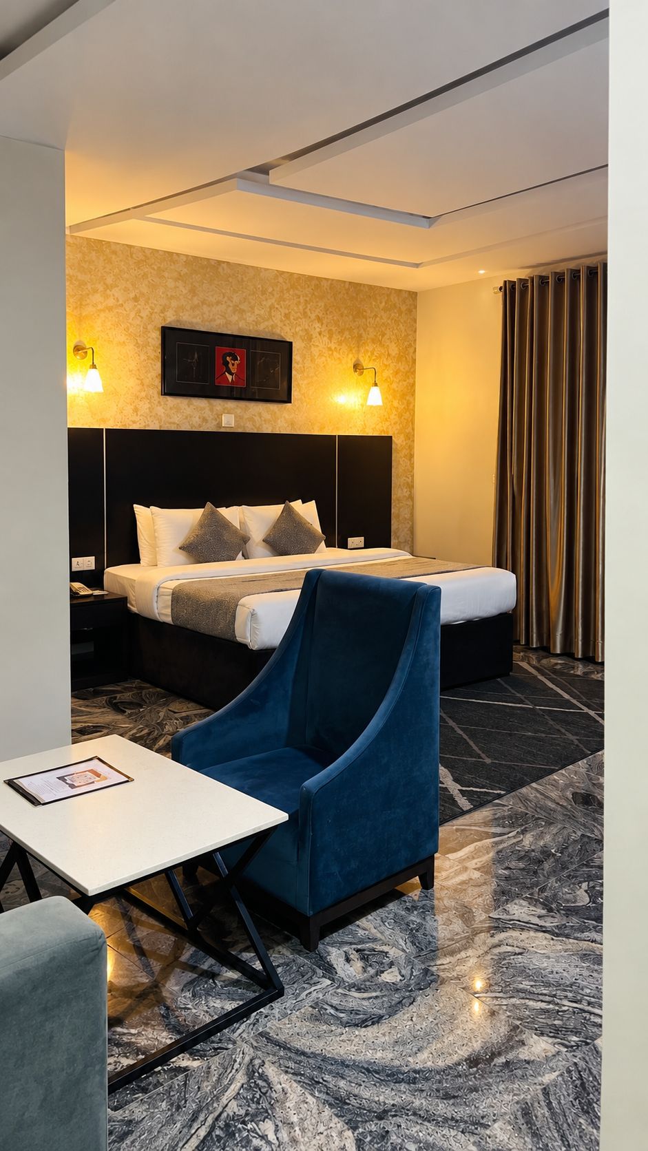 Une chambre d’hôtel avec un lit, une chaise, une petite table et un luminaire fixé au mur.