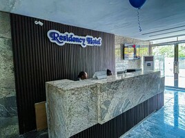 Una recepción con un cartel que dice "Residency Hotel" y un área de piscina al fondo.