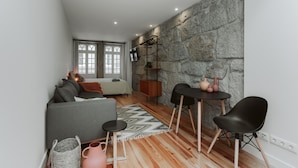 A modern living room with a stone wall, a sofa, a coffee table, and a dining area with chairs. - Casa Farrapos (Porto)