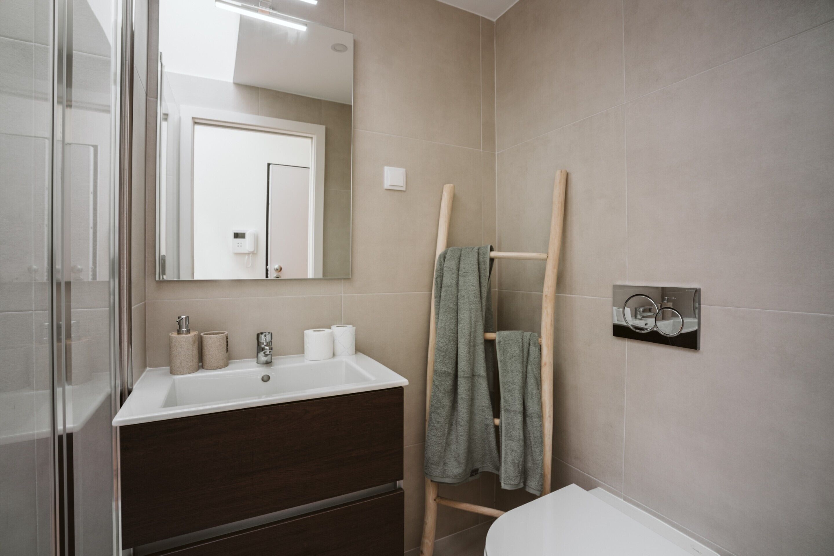 A modern bathroom with a white sink, dark wooden vanity, a glass shower enclosure, and a towel rack with a towel.