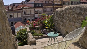 A courtyard with a stone wall, a small table, two chairs, and a variety of plants. - Casa Farrapos (Porto)