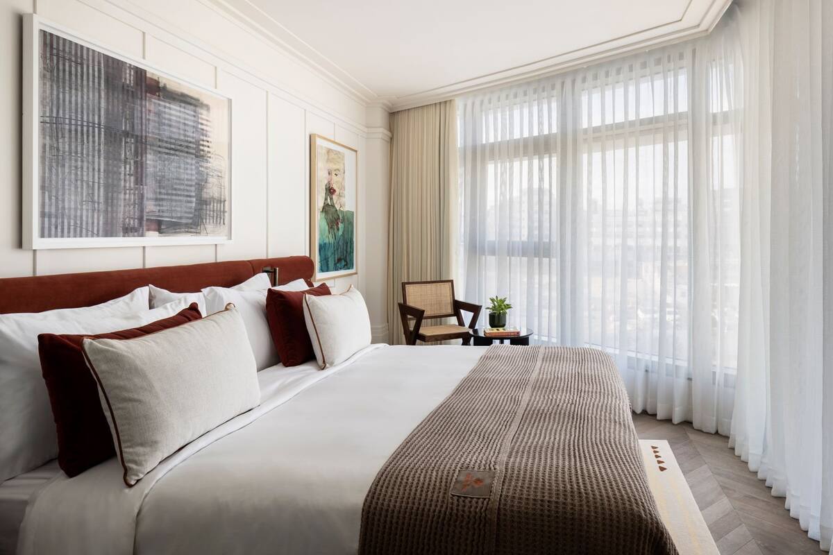 A hotel room with a large bed, a chair, a small table with a plant, and artwork on the walls.