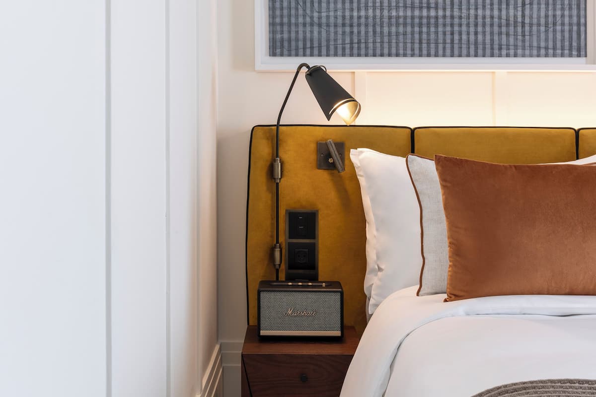 A neatly arranged bedroom with a bed, a bedside table with a lamp, and a framed artwork above the bed.