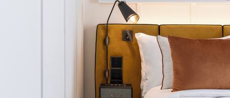 A neatly arranged bedroom with a bed, a bedside table with a lamp, and a framed artwork above the bed.