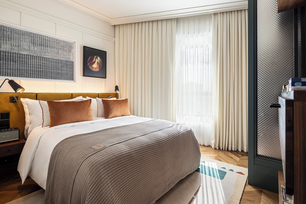 A neatly made bed with a headboard, a bedside table with a lamp, and a large window with sheer curtains.
