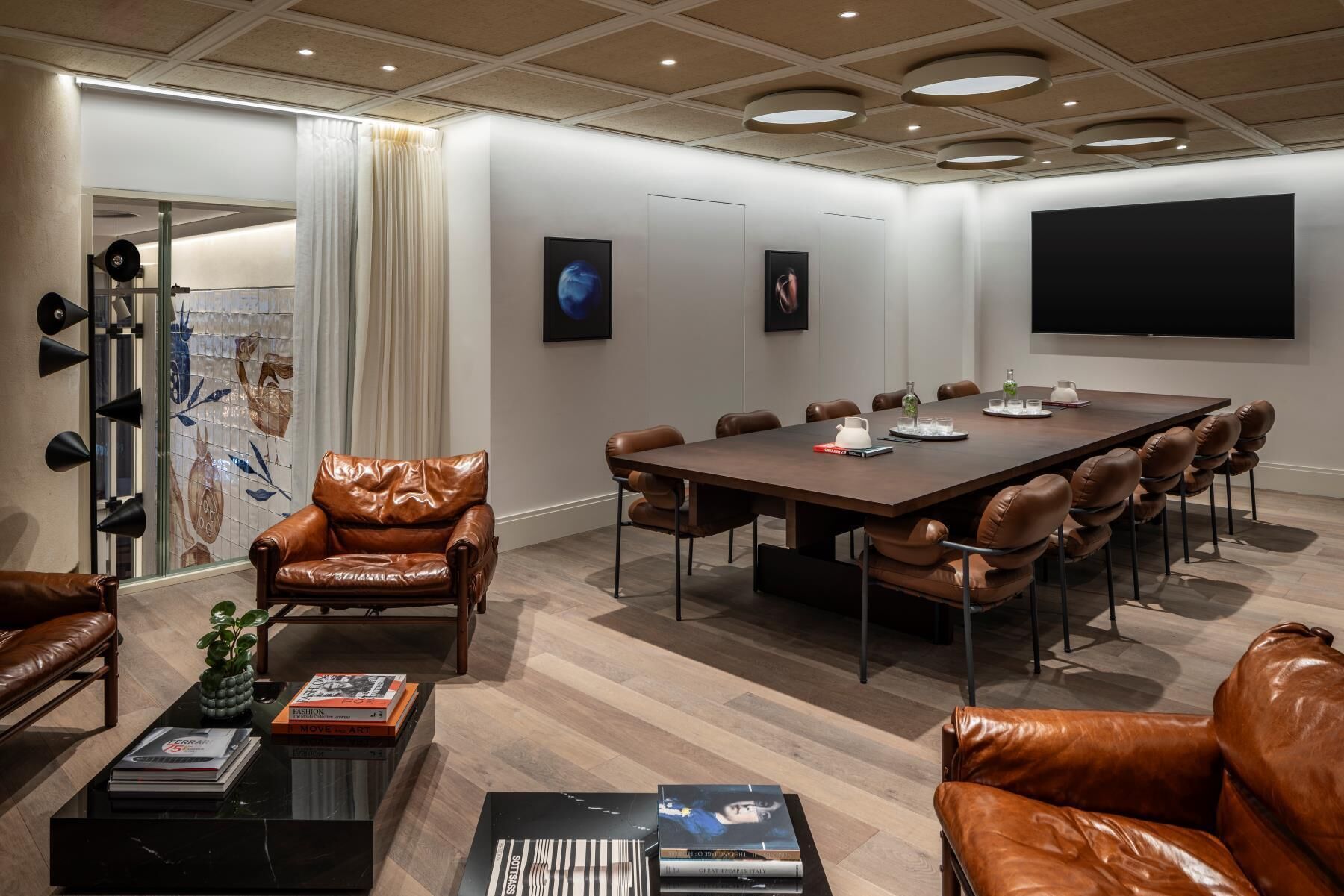 Une salle de conférence avec une longue table, des fauteuils en cuir, un canapé et un écran de télévision.